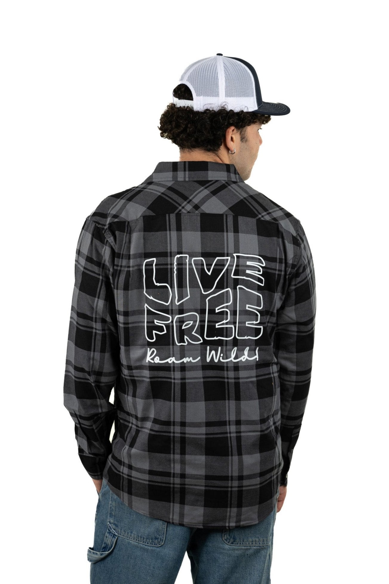 Young man in black unisex plaid Live Free Roam Wild shirt with bold graphic text on the back